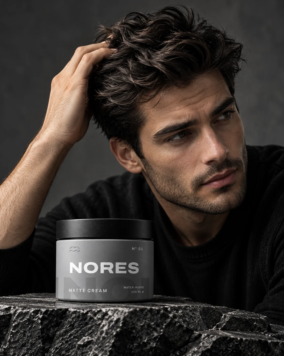 A man with textured, matte-styled dark hair next to a jar of NORES N° 01