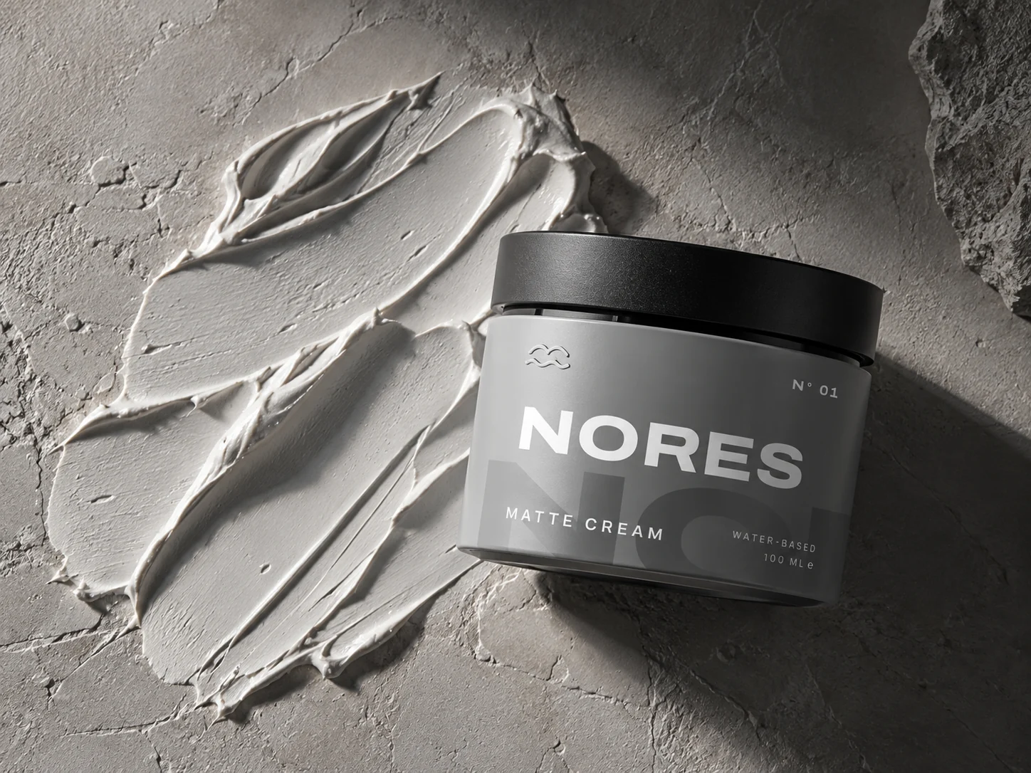 NORES jar lying next to a swipe of matte cream on grey stone